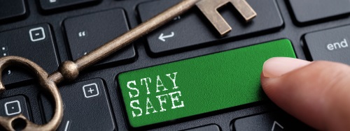 A keyboard with a green button that says "stay safe" almost being pressed by a finger and an old school key lying above it